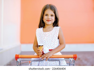 Portrait Happy Little Girl In Shopping Cart With Tasty Ice Cream Having Fun In The City