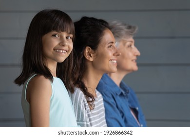 Portrait of happy little Hispanic 7s girl child look at camera smiling, mom and grandmother on background look in distance. Growing generation or small Latino kid with mother and senior grandparent.