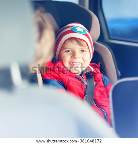 Portrait of happy little kid boy sitting in car. Child in safety car seat with belt. Safe travel with kids and traffic laws concept.
