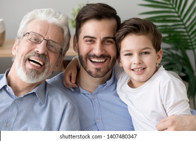 Portrait Of Happy Little Son, Father And Grandfather Sit On Couch Hugging Posing For Family Picture Together, Smiling Three Generations Of Men Embrace Look At Camera Laughing Rest On Sofa At Home