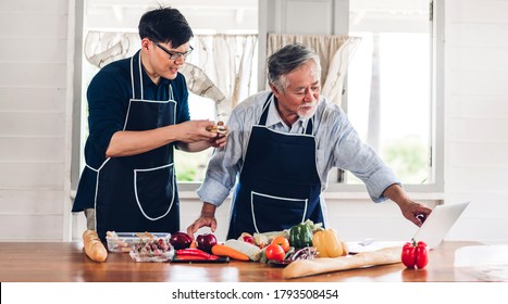 Portrait Of Happy Love Asian Family Senior Mature Father And Young Adult Son Having Fun Cooking Together And Looking For Recipe On Internet With Laptop Computer To Prepare The Yummy Eating Lunch 