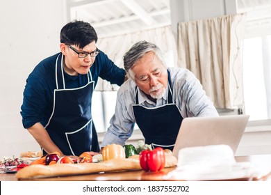 Portrait Of Happy Love Asian Family Senior Mature Father And Young Adult Son Having Fun Cooking Together And Looking For Recipe On Internet With Laptop Computer To Prepare The Yummy Eating Lunch 