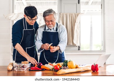 Portrait Of Happy Love Asian Family Senior Mature Father And Young Man Adult Son Having Fun Cooking Food Together And Look For Recipe On Internet With Laptop Computer To Prepare The Yummy Eating Lunch