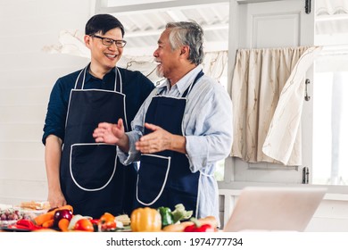 Portrait Of Happy Love Asian Family Senior Mature Father And Young Adult Son Having Fun Cooking Together And Looking For Recipe On Internet With Laptop Computer To Prepare The Yummy Eating Lunch