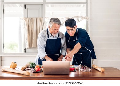 Portrait Of Happy Love Asian Family Senior Mature Father And Young Adult Son Having Fun Cooking Together And Looking For Recipe On Internet With Laptop Computer To Prepare The Yummy Eating Lunch