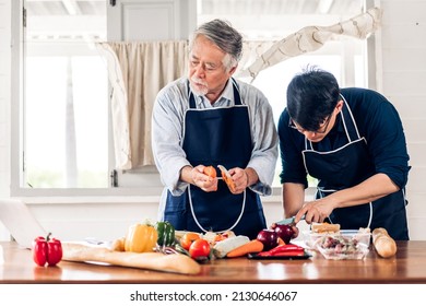 Portrait Of Happy Love Asian Family Senior Mature Father And Young Adult Son Having Fun Cooking Together And Looking For Recipe On Internet With Laptop Computer To Prepare The Yummy Eating Lunch