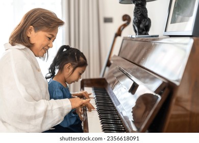 Portrait of happy love asian grandmother and asian cute girl play and enjoy relax teaching and play piano music lesson at home.senior, insurance, care.girl with their laughing grandparents.Family - Powered by Shutterstock