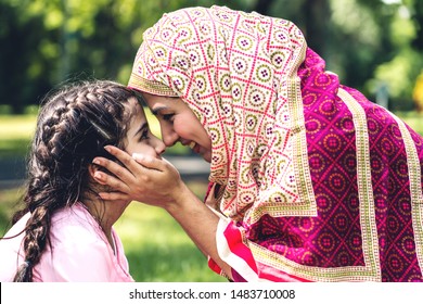 Portrait Of Happy Lovely Family Arabic Muslim Mother And Little Muslim Girls Child With Hijab Dress Smiling And Having Fun Kissing Together In Summer Park