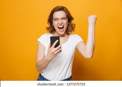 Portrait of a happy lovely girl standing isolated over yellow background, using mobile phone, celebrating - Shutterstock ID 1377275723