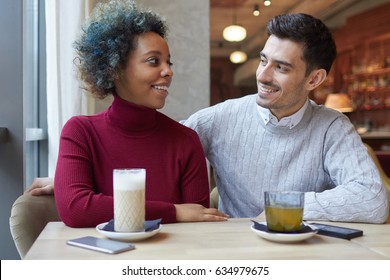 Portrait of happy lovers spending their lunchtime together in small cafe, enjoying their date, coffee and tea, having left phones lying on table, smiling and looking each other in eye with deep love. - Shutterstock ID 634979675