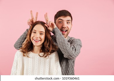 Portrait of happy loving couple dressed in sweaters having fun isolated over pink background