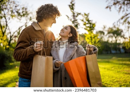 Portrait of happy loving couple in park in sunset. They are looking inside shopping bags.