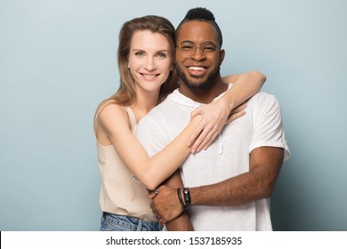 Portrait Of Happy Loving Multiracial Millennial Couple Isolated On Blue Studio Background Hug Looking At Camera, Smiling Multiethnic Man And Woman Embrace Cuddle Posing For Picture Together