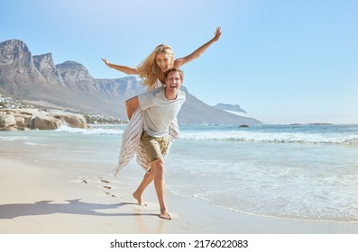 Portrait of a happy and loving young couple enjoying a day at beach in summer. Cheerful affectionate husband giving his joyful wife a piggyback while walking and having fun by the seashore on holiday - Powered by Shutterstock