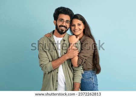 Portrait of happy loving young eastern couple embracing and smiling at camera isolated on blue studio background. Beautiful millennial indian lady embracing her handsome boyfriend