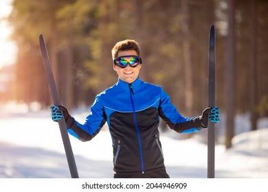 Portrait happy male athlete with cross country skis in hands and goggles, training in snowy forest. Healthy winter lifestyle concept.