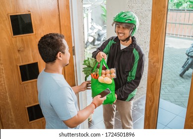 Portrait Of Happy Male Courier Delivering Online Grocery Shopping To Customer At Home