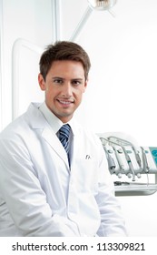 Portrait Of Happy Male Dentist Sitting In Clinic