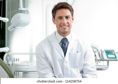 Portrait Of Happy Male Dentist Wearing Lab Coat While Sitting In Clinic