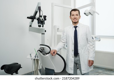 Portrait Of Happy Male Dentist Wearing Lab Coat In White Dental Clinic