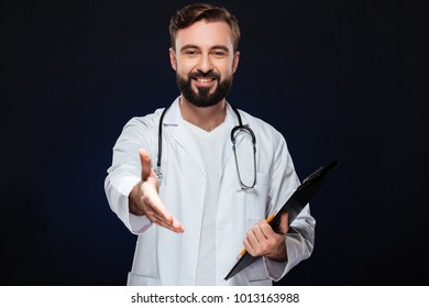 Portrait Of A Happy Male Doctor Dressed In Uniform With Stethoscope Standing With Outstretched Hand For Greeting Notepad Isolated Over Dark Background