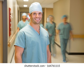 Portrait of happy male doctor with team in background at hospital corridor