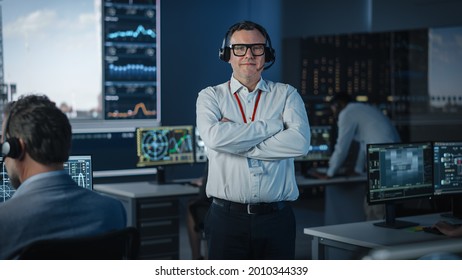 Portrait of a Happy Male Flight Controller Posing for Camera in a Mission Control Center. Successful Man Wearing a Headset and a White Shirt. Computer Screens in the Background. - Powered by Shutterstock