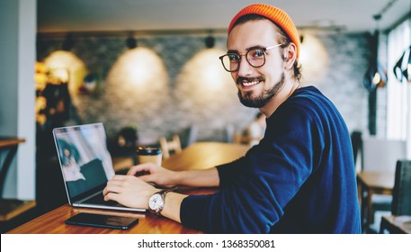 Portrait Of Happy Male Freelancer In Optical Eyewear Smiling At Camera During Break From Working Online, Positive Cheerful Hipster Blogger Sitting On Publicity Area With Modern Laptop Computer