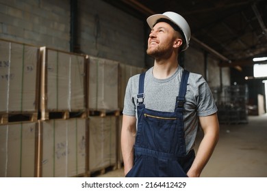 Portrait Of Happy Male Worker In Warehouse With White Helmet Standing Between Shelves