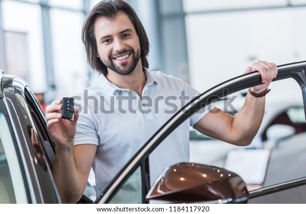 portrait of happy man with car key standing at new\
car in dealership\
salon