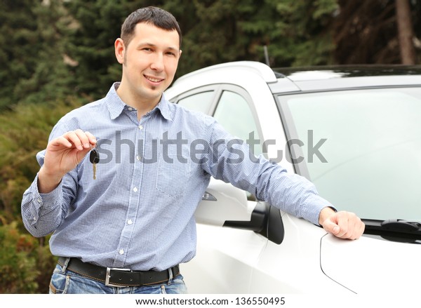 Portrait\
of happy man with car key, standing near the\
car