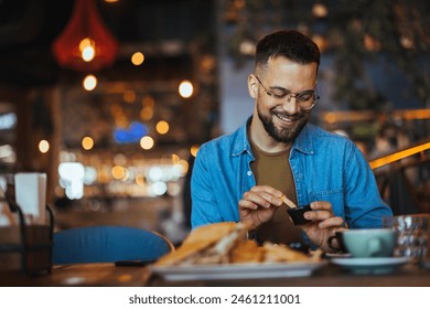 Portrait of a happy man eating at a restaurant and smiling - lifestyle concept. A young man with a beard sitting in a restaurant and holding hands french fries and going to eat