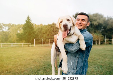 Portrait Of Happy Man Holding His Friend Dog Labrador At Sunset In Park