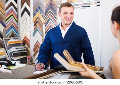 Portrait Of Happy Man Seller Taking Order On Picture Frame From Customer At Counter In Store 