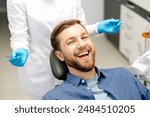 Portrait of happy man sitting at dentist chair in modern clinic and smiling. Patient enjoying dental treatment with professional dentist.