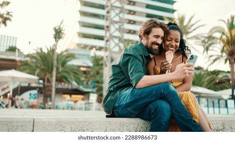 portrait of happy man and smiling woman watching video on smartphone. Close-up of joyful young interracial couple browsing photos on mobile phone on urban city background - Powered by Shutterstock