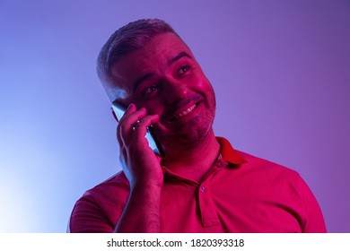 Portrait Of Happy Man Talking On Phone With Neon Light. Smiling Casual Man Talking On Smartphone At Gel Studio Light.