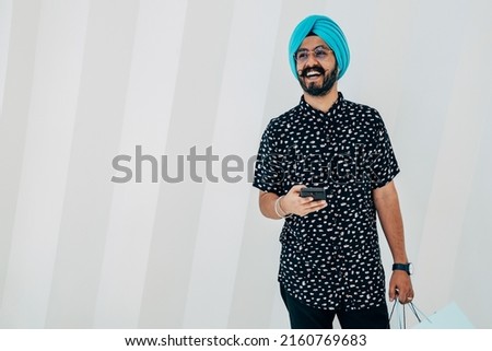 Portrait Of A Happy Man Using Mobile Phone And Holding Shopping Bags While Standing In Front Of White Background