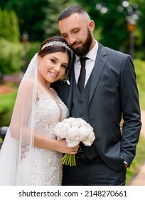 Portrait of happy married couple, wearing in vogue wedding outfits, standing together outdoor, smiling and posing at camera during wedding day
