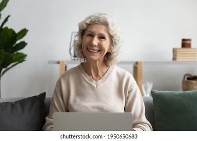 Portrait Of Happy Mature 60s Woman Using Laptop At Home, Looking At Camera, Smiling. Senior Lady Posing While Talking To Doctor Online, Making Video Call, Watching Webinar. Head Shot, Screen View