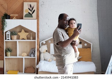 Portrait Of Happy Mature African American Dad Holding Lovely Baby Daughter Taking Selfie Photos On Smartphone Camera