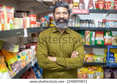 Portrait of happy mature beard Indian man wearing shirt standing cross arm at grocery shop or supermarket, Closeup. Selective Focus.
