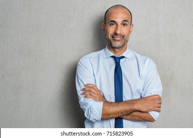 Portrait Of Happy Mature Businessman Standing Against Grey Background While Looking At Camera. Proud Senior Business Man Against Grey Wall With Copy Space. Executive Manager With Arms Crossed Smiling.