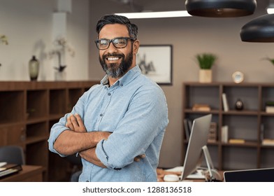 Портрет счастливого зрелого бизнесмена носить очки и смотреть на камеру. Многоэтнический довольный человек чувствует себя уверенно в творческом офисе. Успешный ближневосточный бизнесмен улыбается.