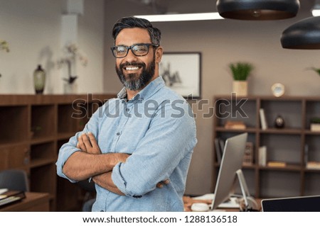 Portrait of happy mature businessman wearing spectacles and looking at camera. Multiethnic satisfied man  feeling confident in a creative office. Successful middle eastern business man smiling.