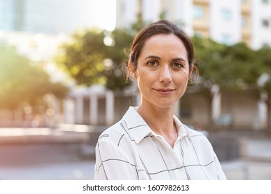 Portrait of happy mature businesswoman looking at camera. Successful proud woman in city street at sunset. Satisfied latin business woman in formal clothing smiling outdoors.
