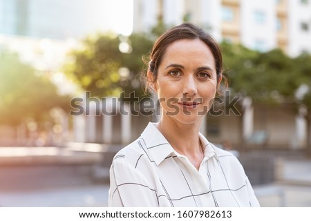 Portrait of happy mature businesswoman looking at camera. Successful proud woman in city street at sunset. Satisfied latin business woman in formal clothing smiling outdoors.