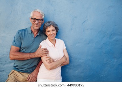 Portrait Of Happy Mature Couple Standing Together Against Blue Wall. Middle Aged Man And Woman Looking At Camera And Smiling On Blue Background