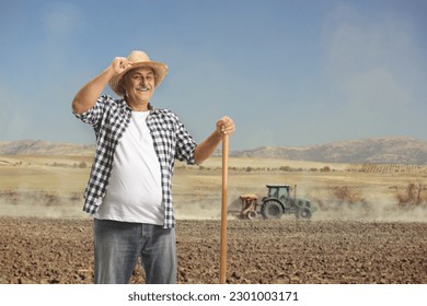 Portrait of a happy mature farmer with a shovel standing on a dusty field with tractor