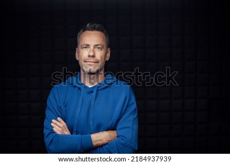 Portrait of happy mature man with arms crossed standing in studio with dark background and looking at camera.